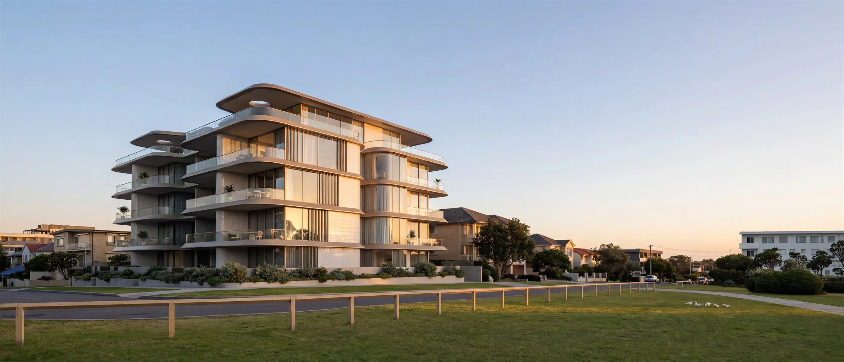 Five-storey Coogee apartment building seen across the parkland, its curved balconies and sculpted roof stepping above native coastal planting within the surrounding residential streetscape