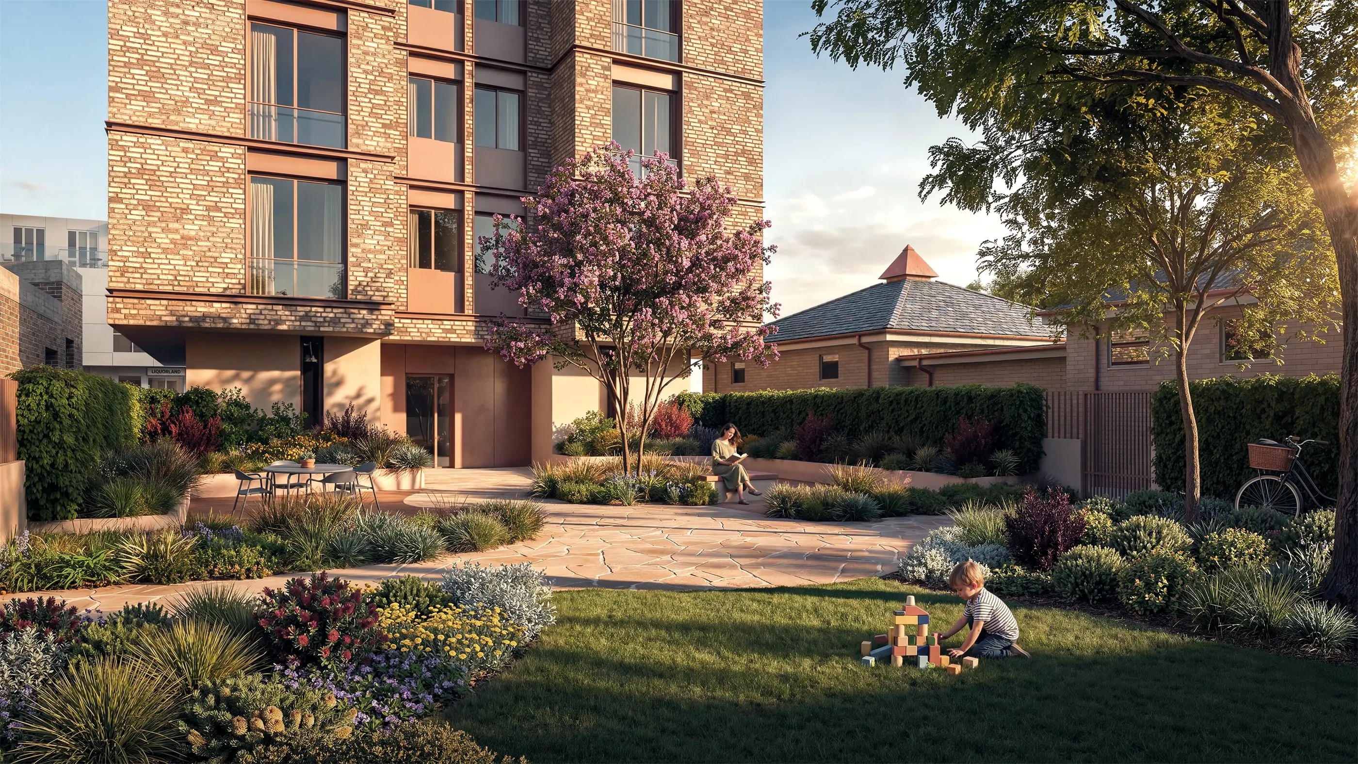 The communal courtyard at Five Dock in summer, a flowering crepe myrtle above sandstone paving, native garden beds, curved rendered seating walls and lawn beneath the brick apartment building.