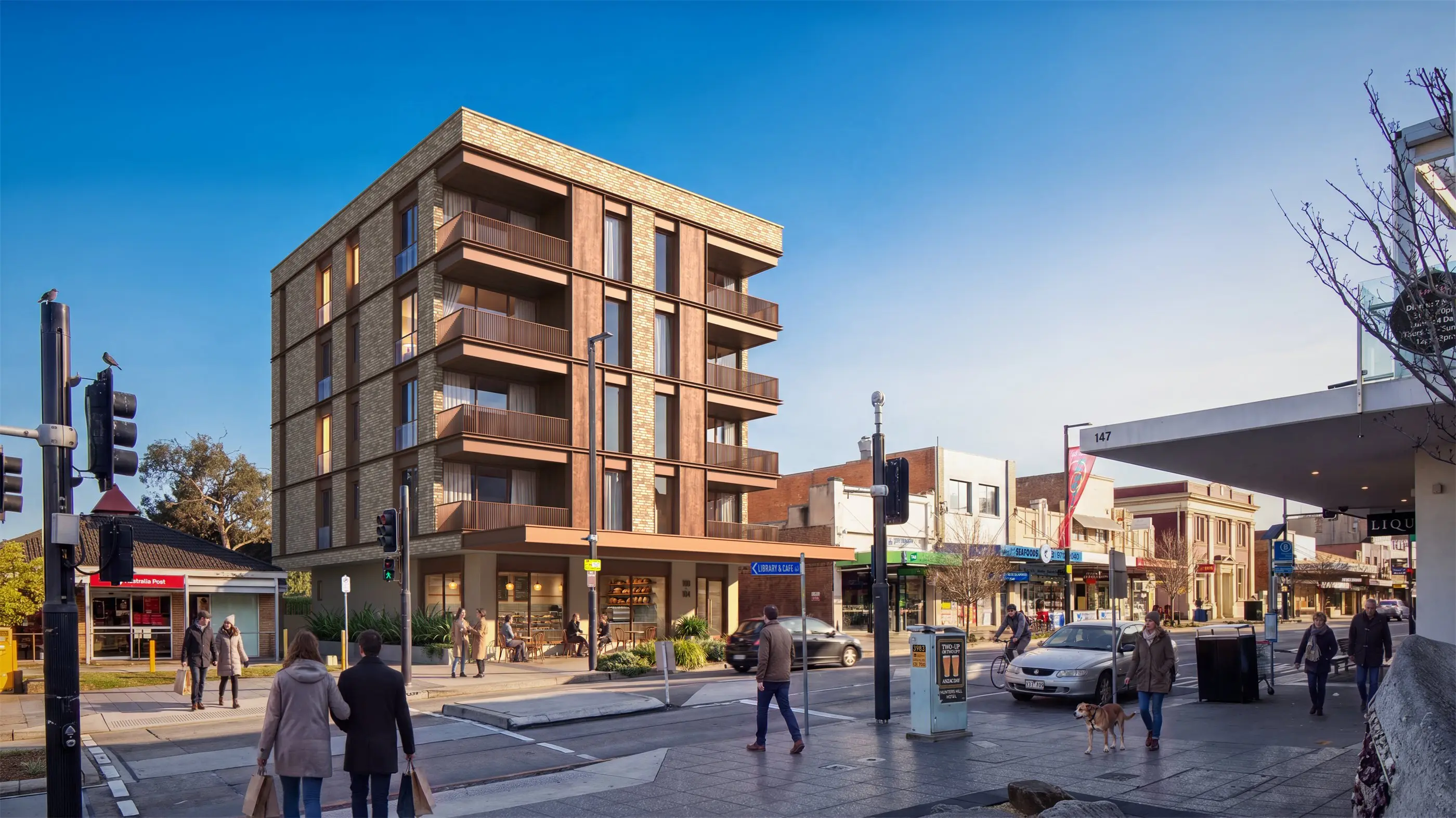 Corner view of the Five Dock apartments on a clear winter morning, four residential levels of recessed balconies above a glazed café tenancy, with the post office and neighbouring shopping strip alongside.